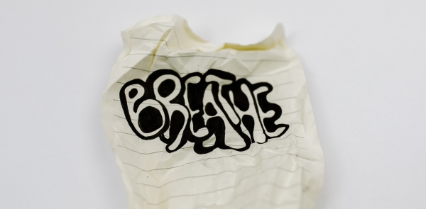 A crumpled up sheet of lined paper with the word "Breathe" written artistically with a black marker
